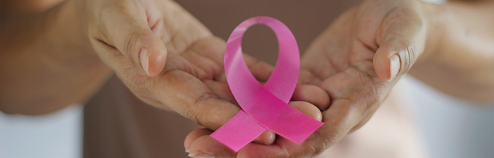 Foto e mãos abertas que se sobrepõem e em cima das mãos está um laço rosa em apoio ao outubro rosa