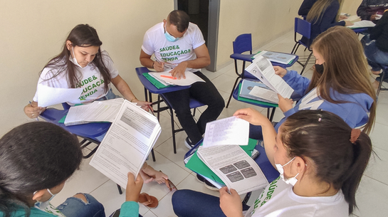 Foto de pessoas sentadas em uma roda lendo textos em papel