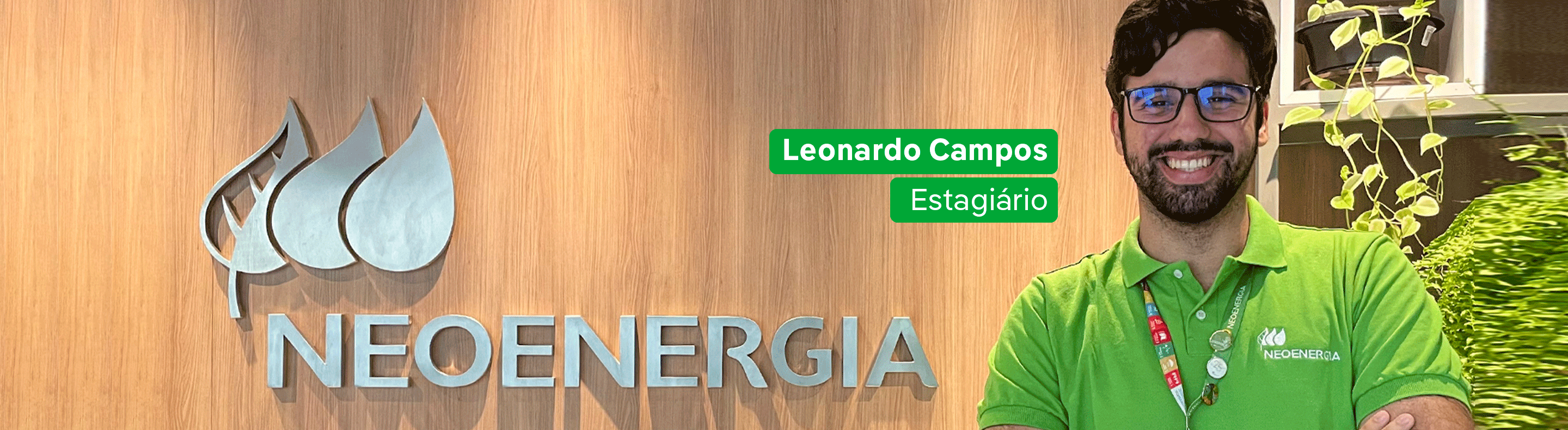 Estagiário da Neoenergia Coelba com camisa verde da empresa em frente a um letreiro com nome Neoenergia.
