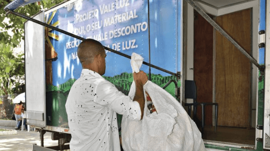 Foto de homem segurando saco com itens recolhidos e entrando em caminhão do Projeto Vale Luz